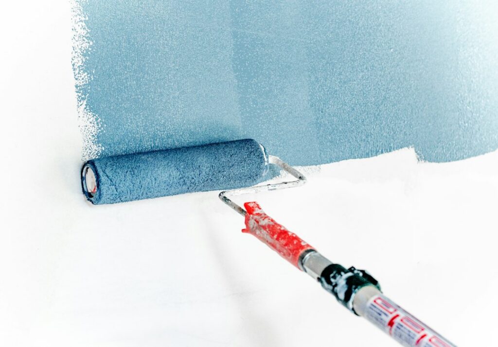 Paint roller on an extension pole applying a coat to a wall, showing the roller technique used when applying epoxy paint