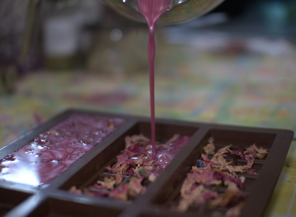 Pink coloured epoxy being poured into a tray, one of many resin molds used for casting